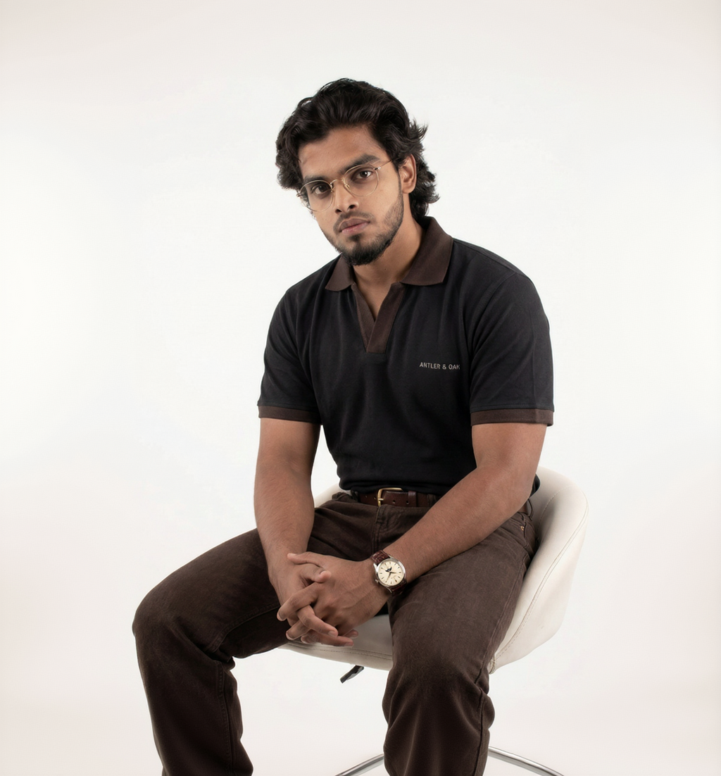 Man wearing a black polo shirt and brown pants sitting on a white chair against a white background