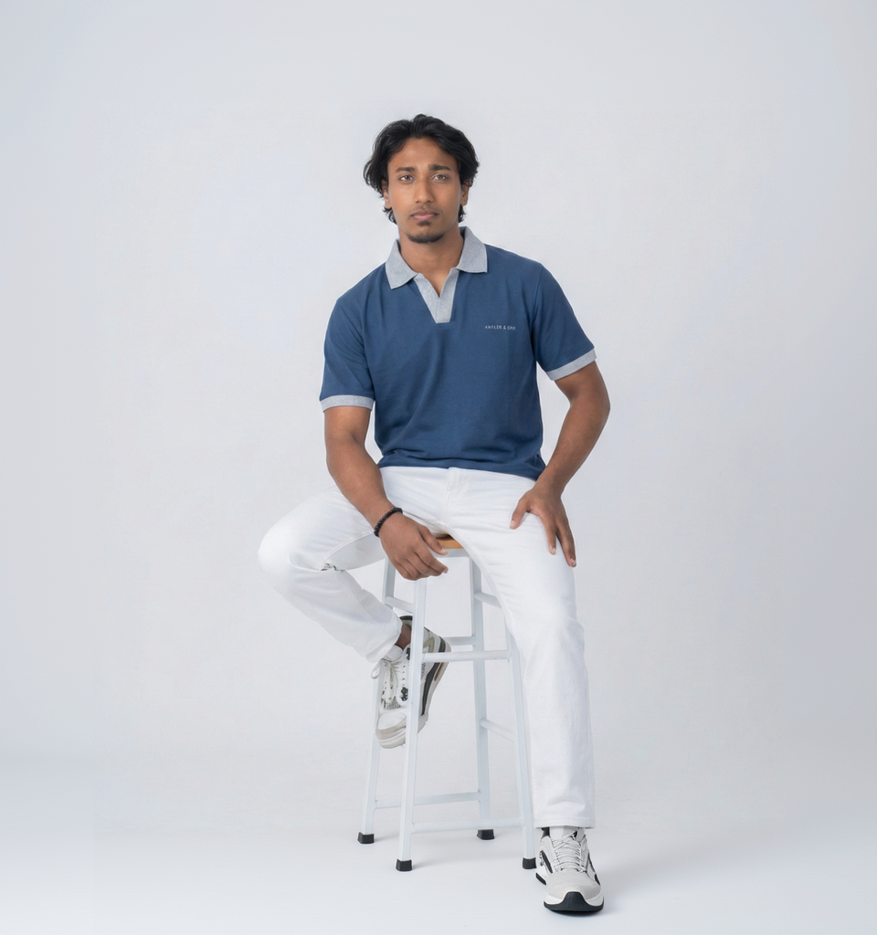 Man sitting on a stool wearing a blue polo shirt and white pants against a white background