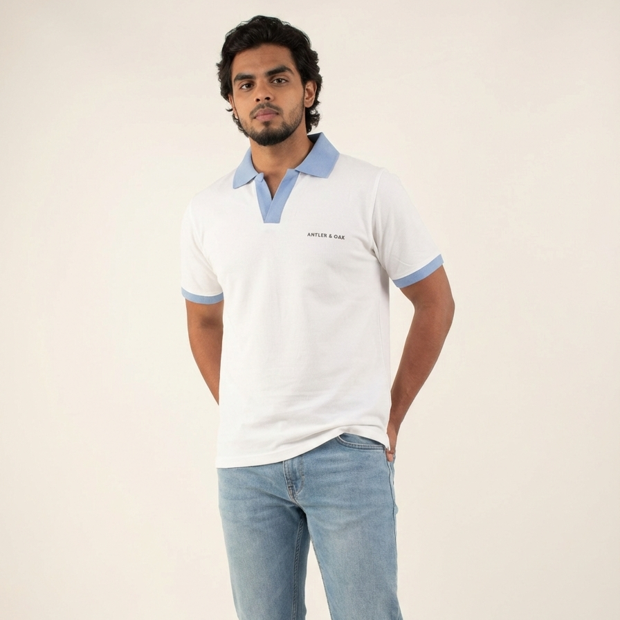 Man wearing a white polo shirt with blue accents and light blue jeans on a plain background