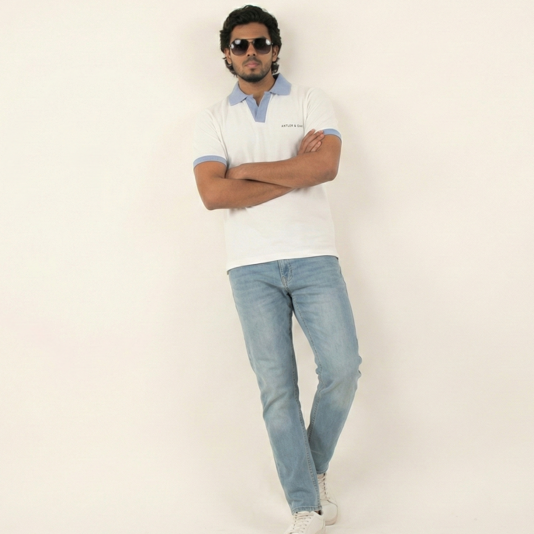 Man wearing a white polo shirt and light blue jeans against a plain background